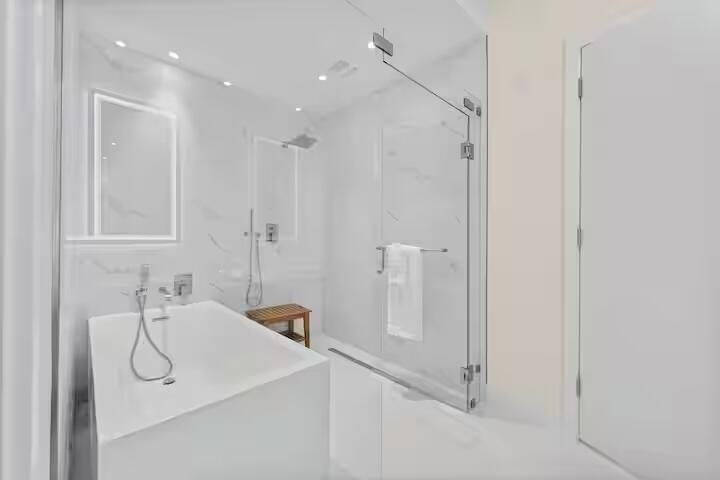Freestanding soaking tub with floor-mounted fixtures, frameless glass shower enclosure, and white tile surround