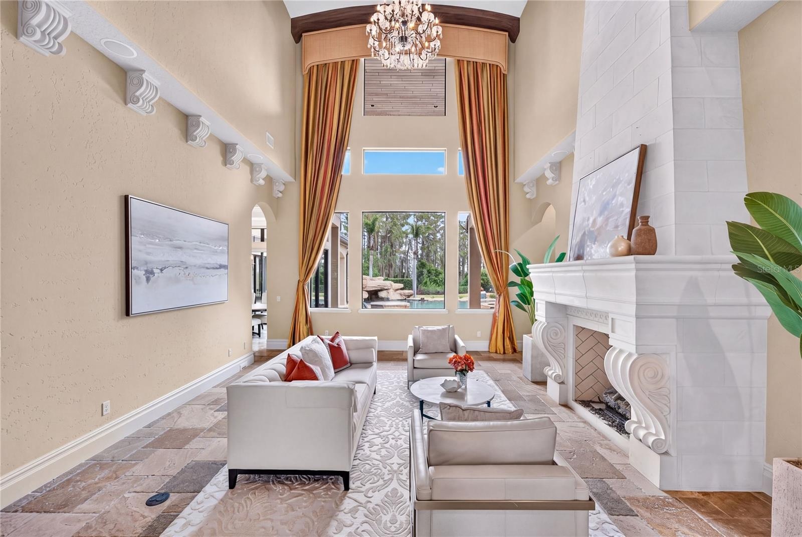 The foyer opens to a two-story travertine-tiled formal living area with dramatic fireplace and towering picture windows that frame the view of the poo