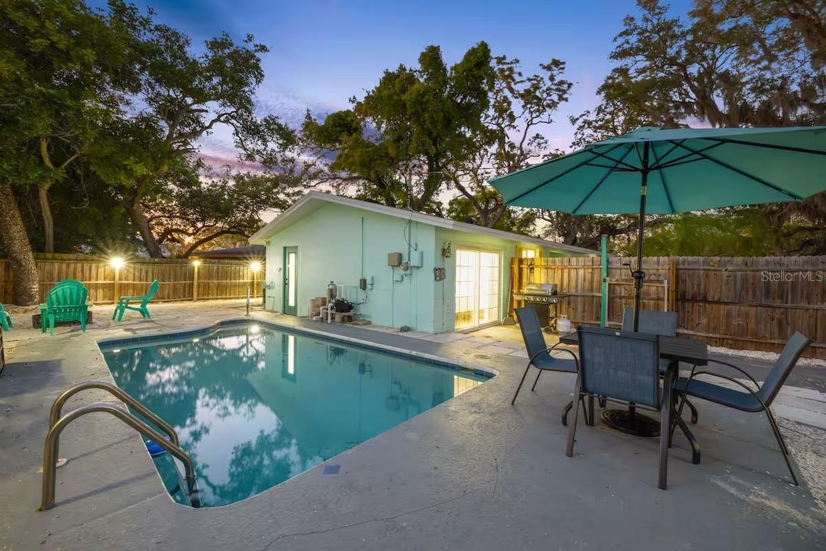 Evening lighting shows off the backyard’s resort-like setup, complete with heated pool, outdoor dining, BBQ area, and space to gather around the fire 