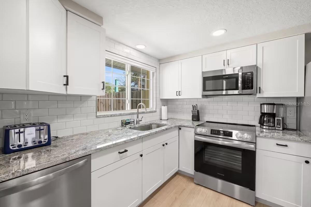 Crisp white cabinetry, stainless steel appliances, granite counters, and subway tile create a bright, fresh kitchen with plenty of workspace and stora