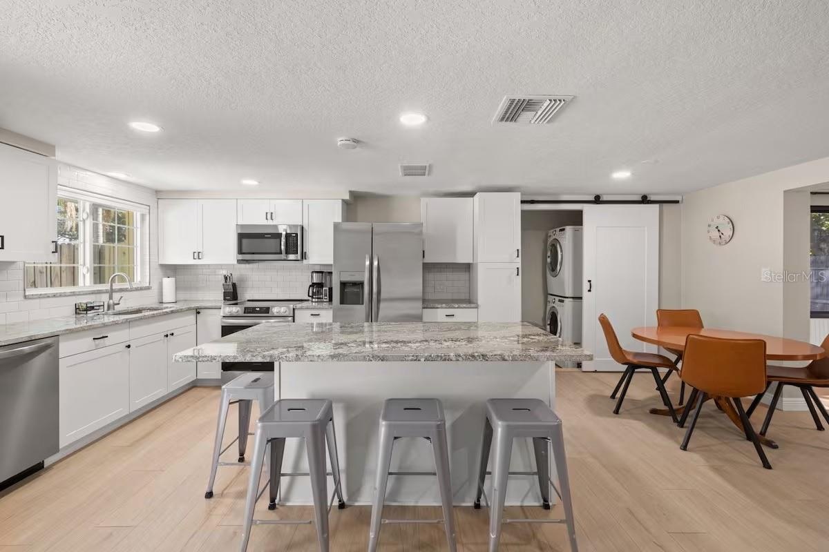 Another view highlights the generous island, open dining area, and convenient tucked-away laundry—all seamlessly connected to the main living spaces.