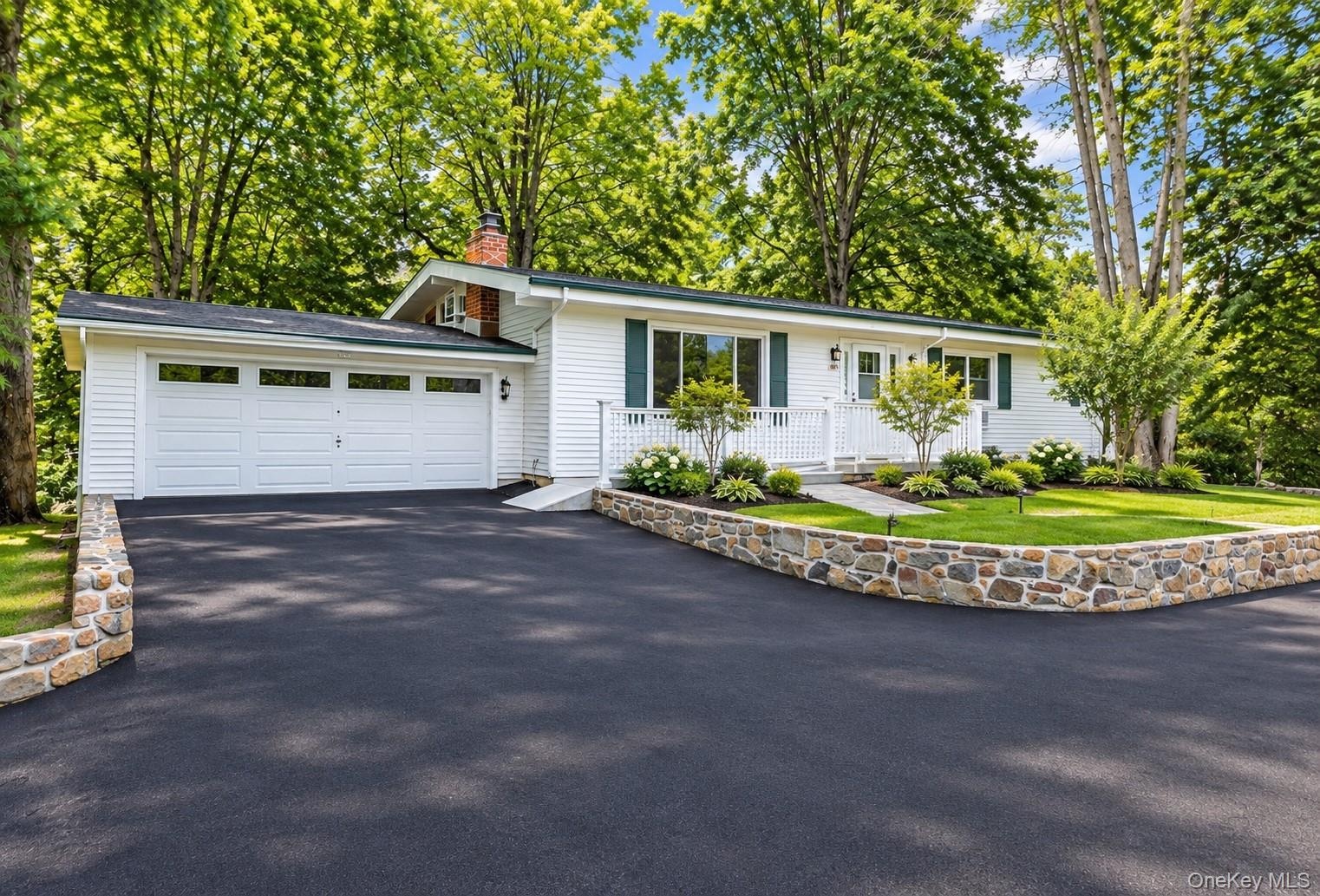 White siding exterior with a two-car garage, brand new asphalt driveway, and a stone retaining wall