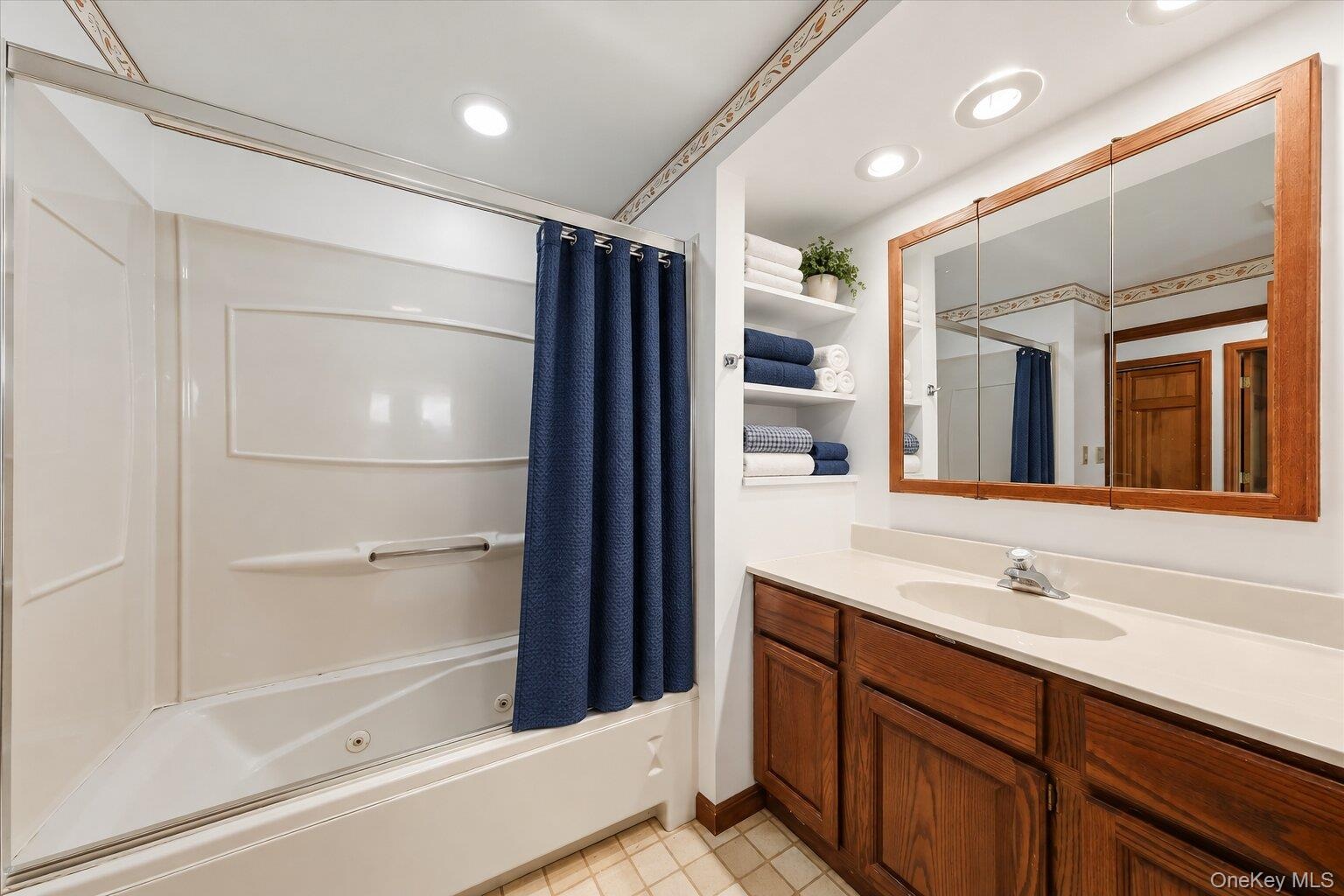 Full bathroom featuring a tub/shower combination, spacious vanity, built-in shelving, and generous mirror space.