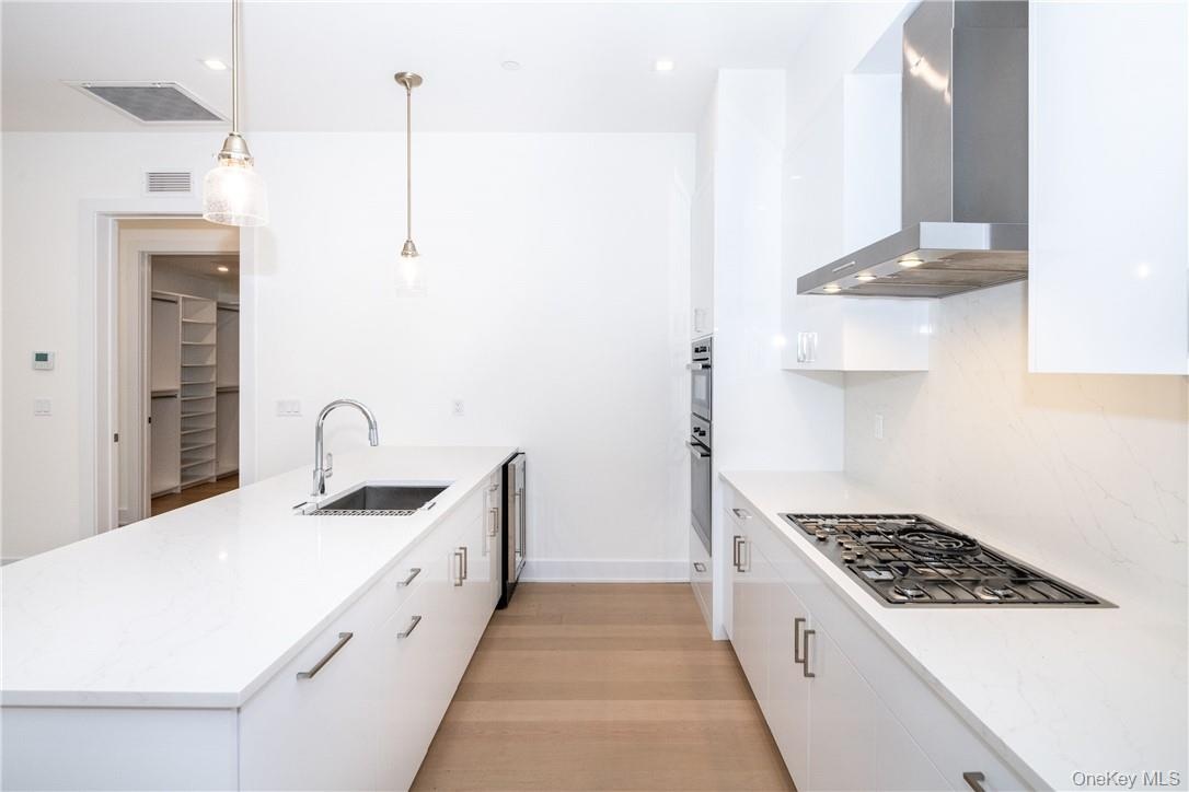 Kitchen featuring stainless steel appliances, wall chimney range hood, decorative light fixtures, white cabinets, and light hardwood / wood-style floo