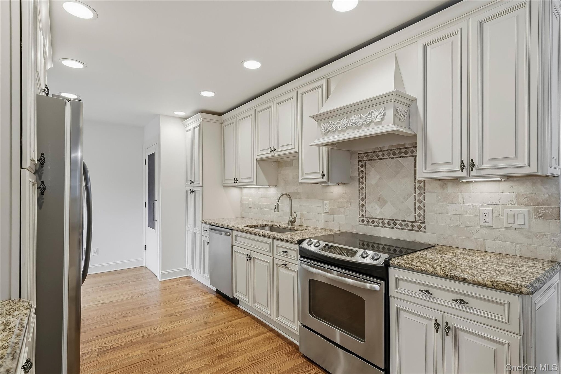 Elegant white kitchen w/ pantry, granite countertops, & custom cabinetry.
