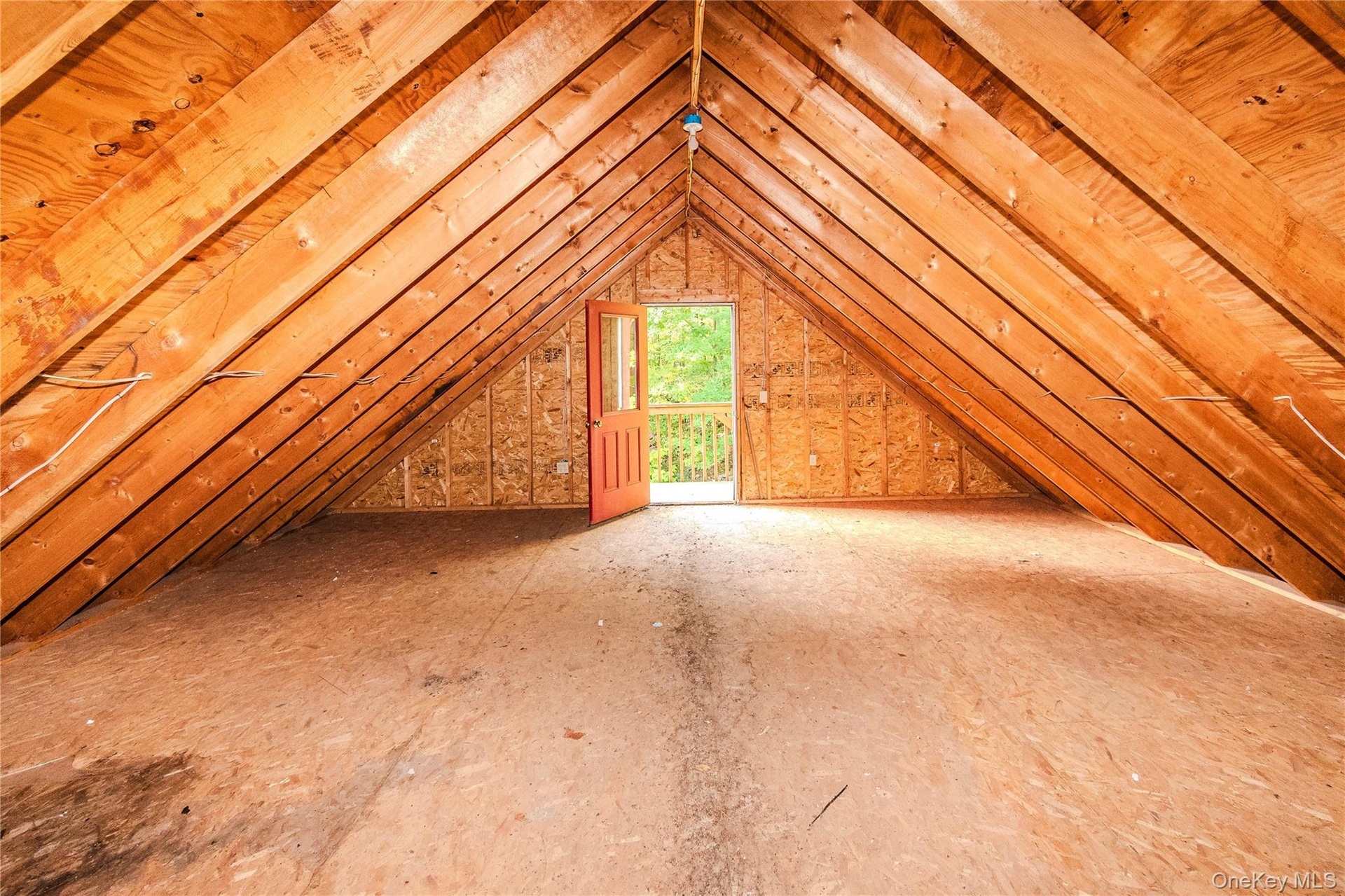 Vaulted wood beam ceiling, exposed wood rafters, wood paneling, open doorway, and outdoor balcony with railing