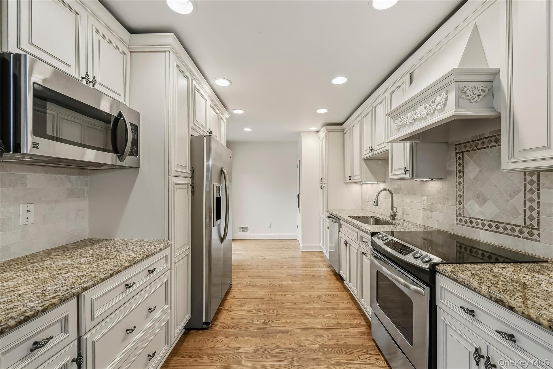 Elegant white kitchen w/ pantry, granite countertops, & custom cabinetry.