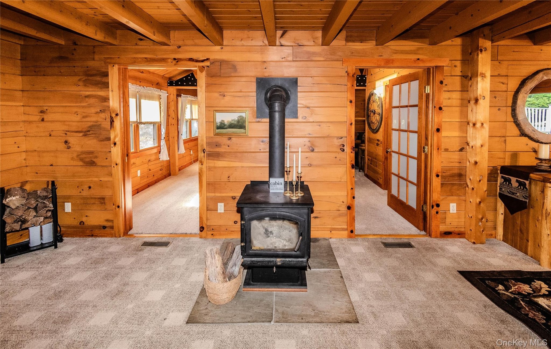 Wood paneling throughout, exposed wood beam ceiling, central wood-burning stove, and two frosted glass French doors