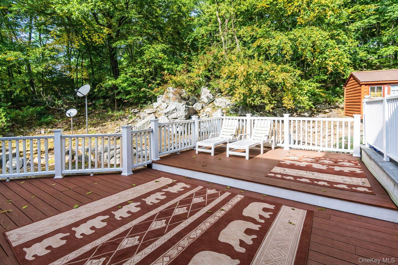 Multi-level outdoor deck with composite decking and white railing, surrounded by natural rock formations and mature trees