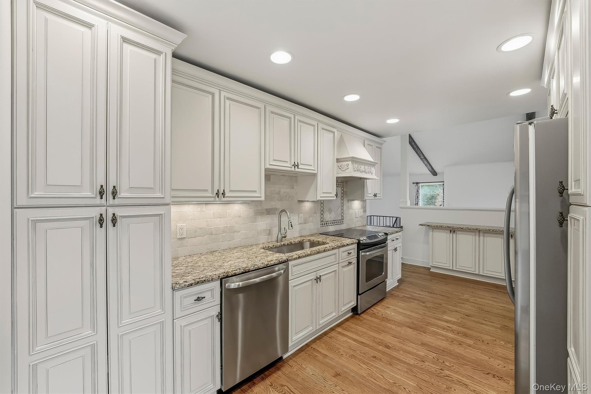 Elegant white kitchen w/ pantry, granite countertops, & custom cabinetry.
