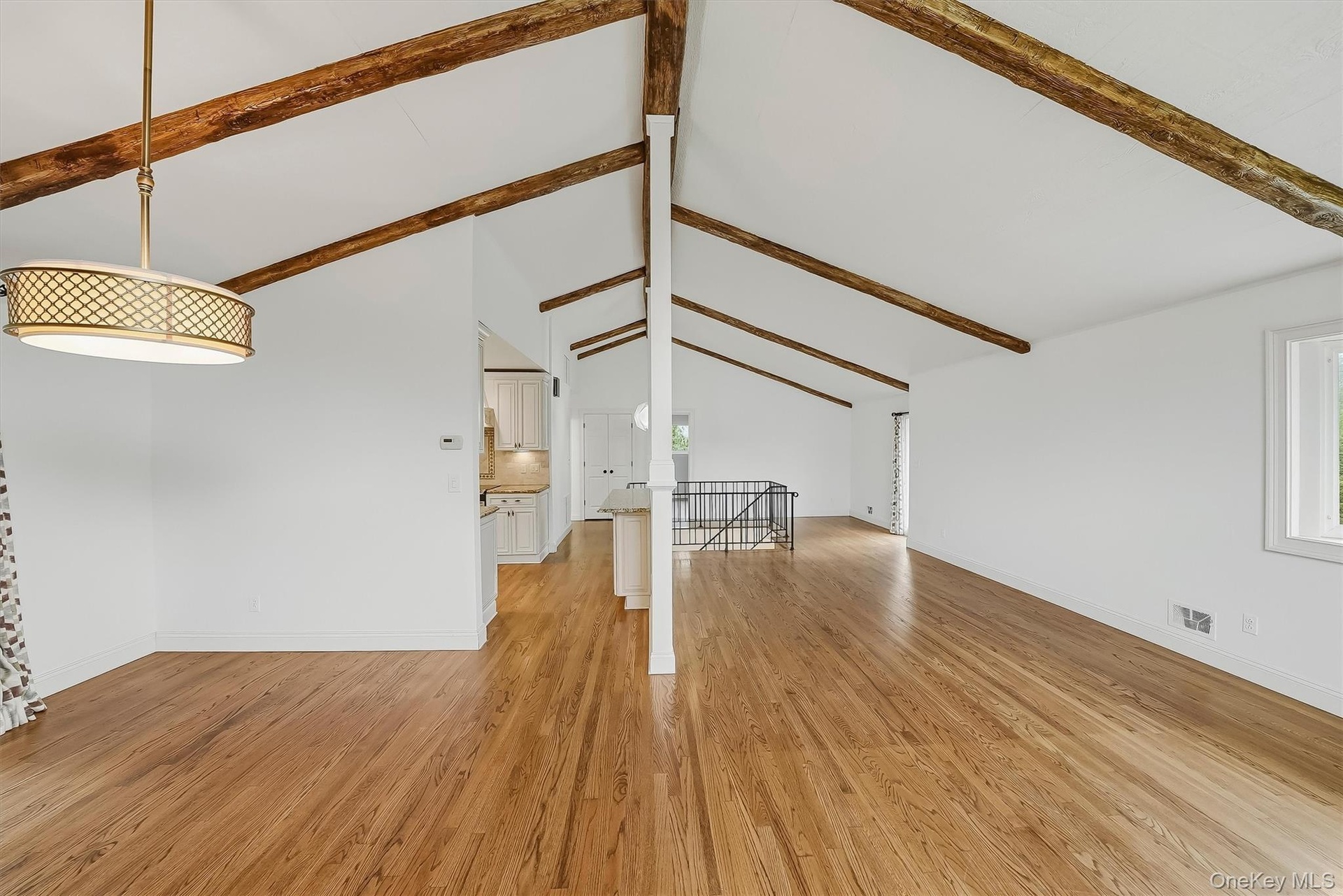 Open-plan great room w/ hardwood floors, exposed wood beams, and fresh paint.