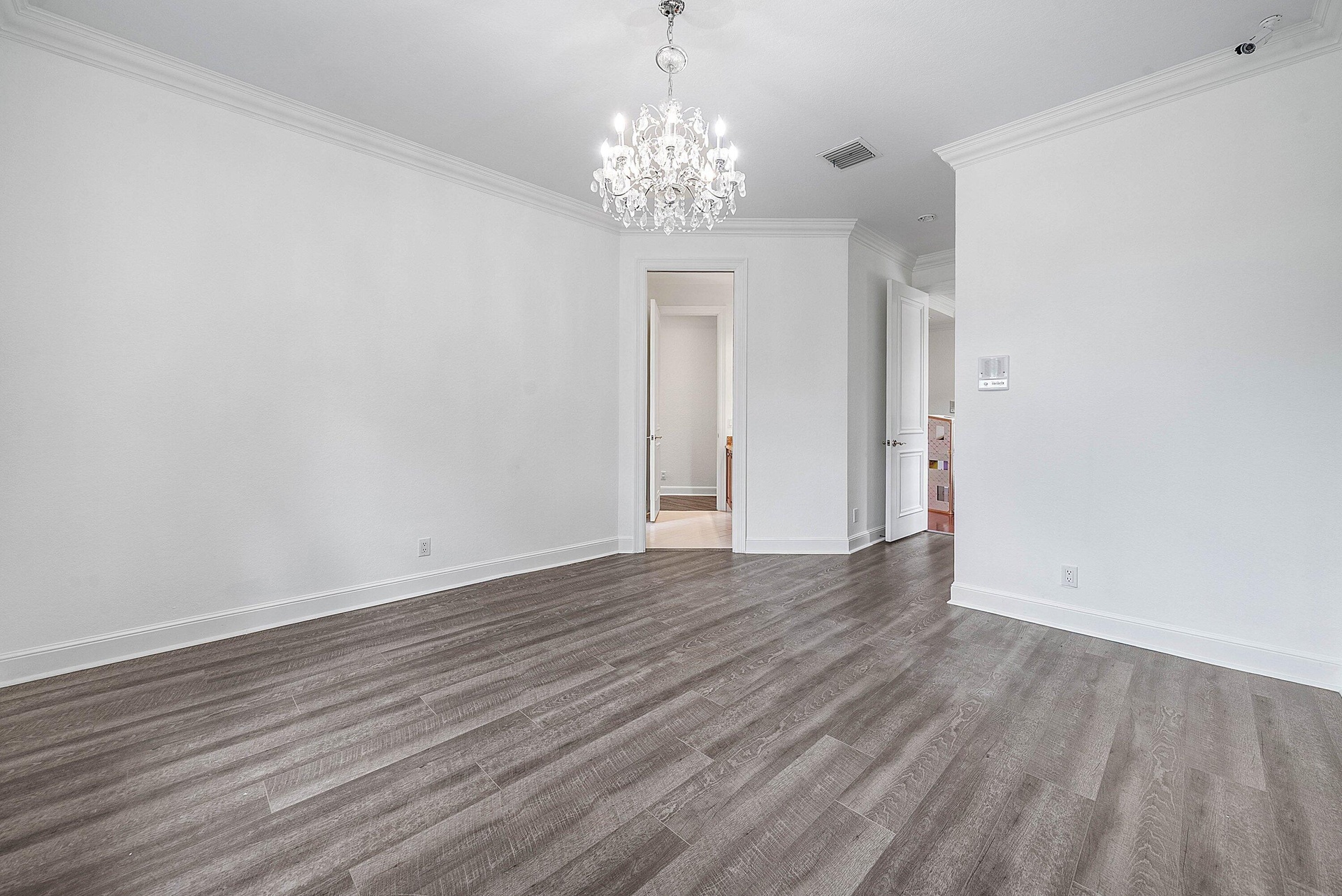Wood-finish flooring, crown molding, white paneled doors leading to shared bathroom