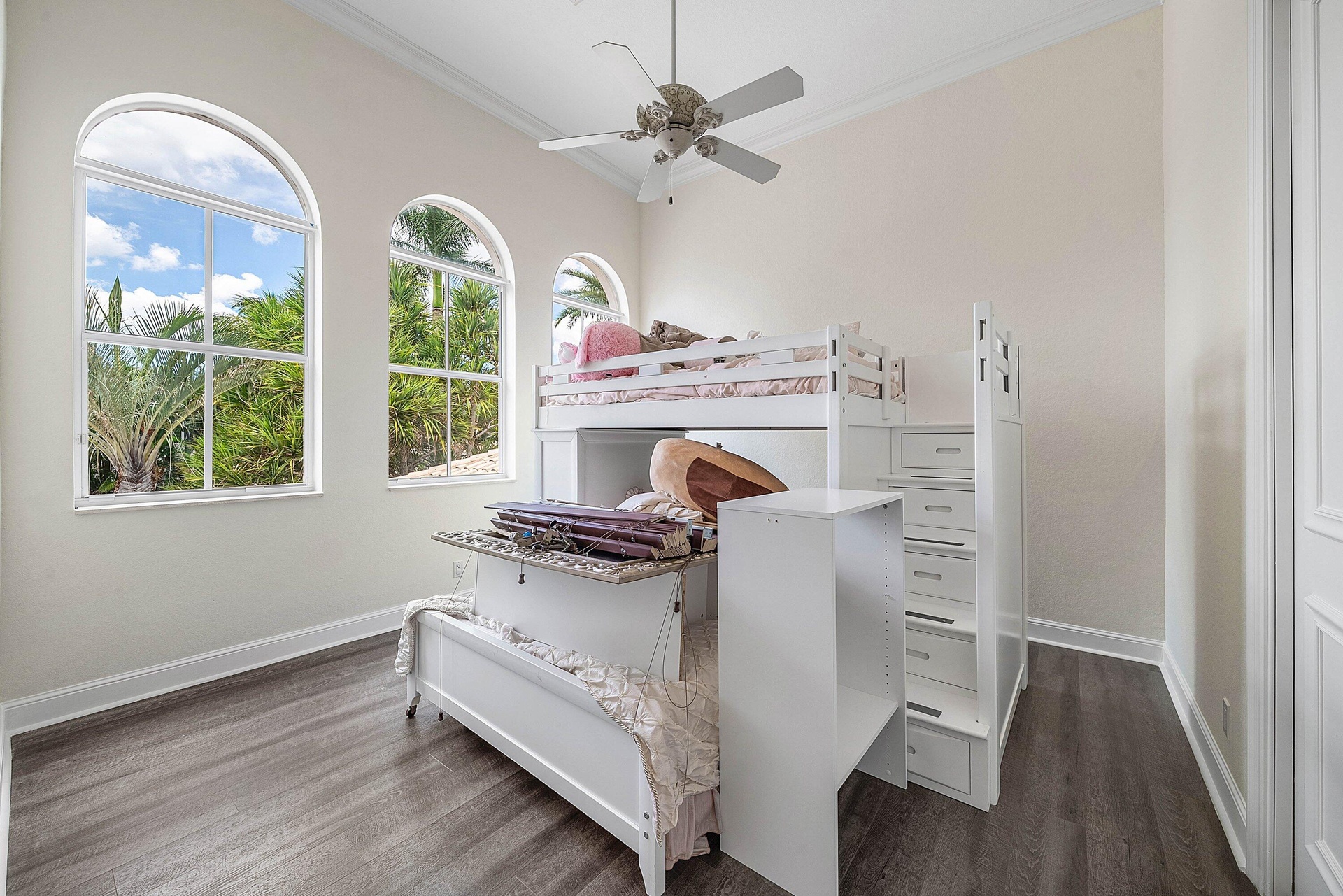 Vaulted ceiling with a ceiling fan, arched windows, and wood-finish flooring