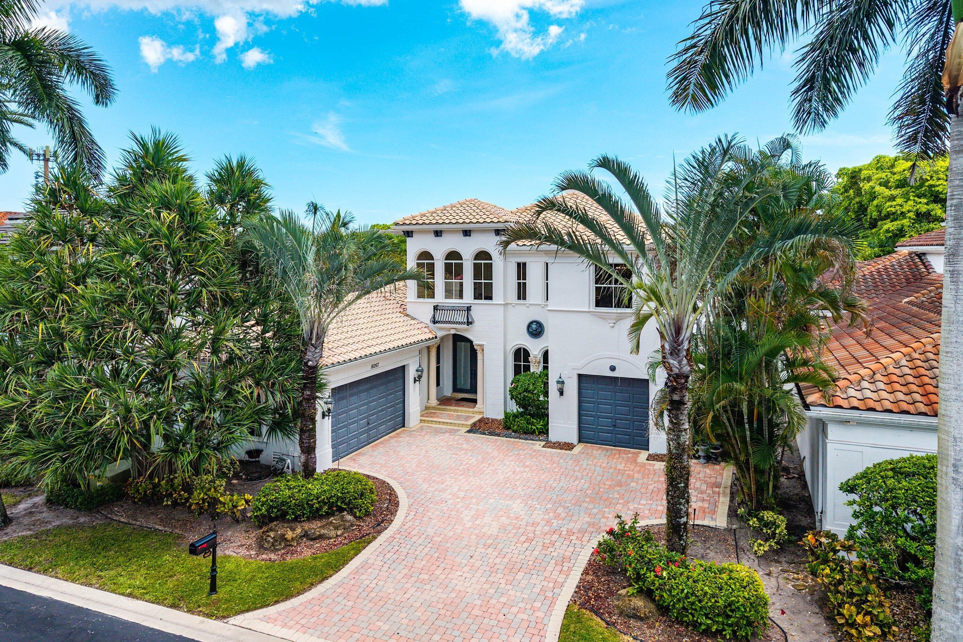 Mediterranean-inspired architecture, modern color palette, with a barrel tile roof, arched windows, a paver driveway, and mature landscaping