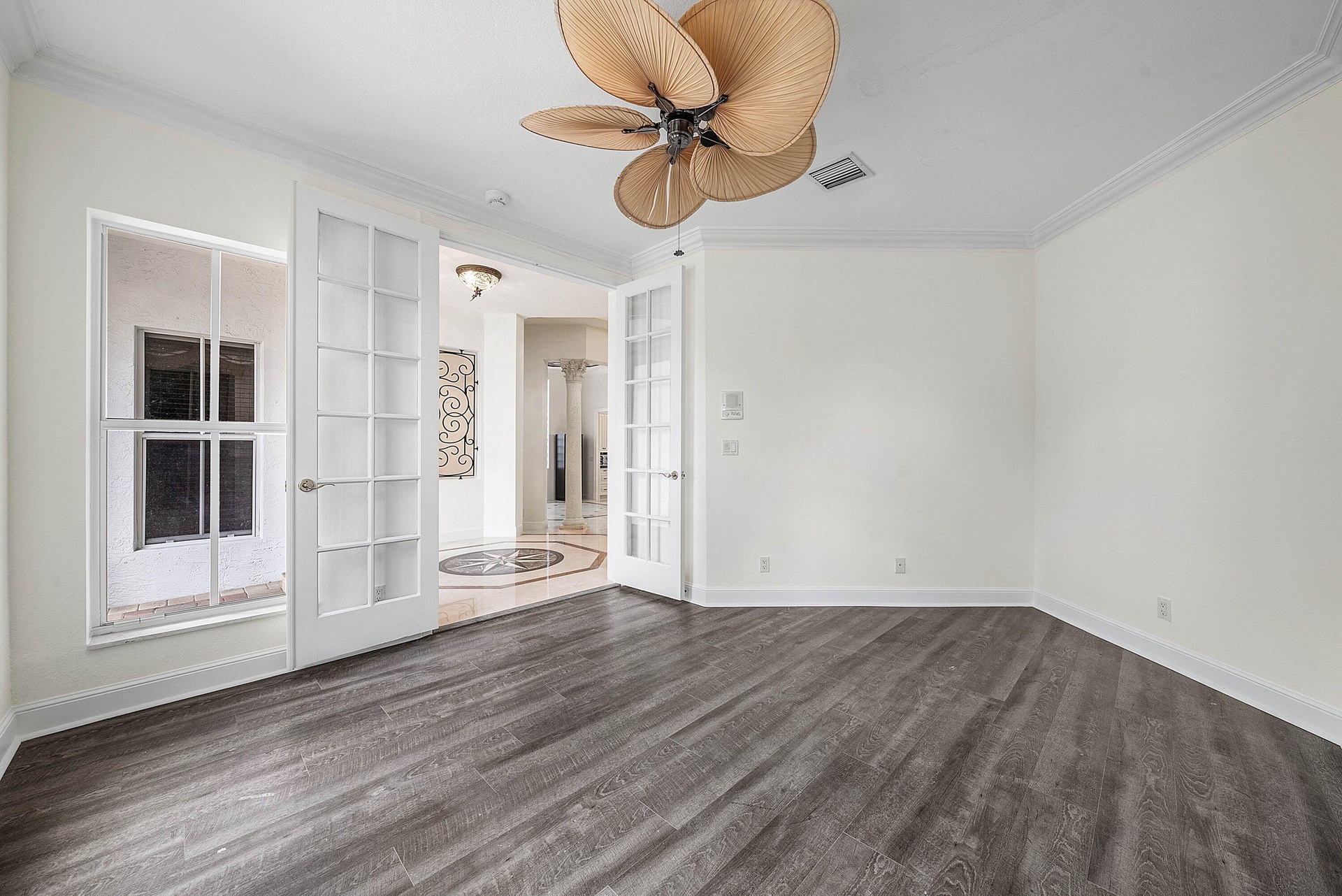 Wood-finish flooring, crown molding, double French doors, large window, and ceiling fan