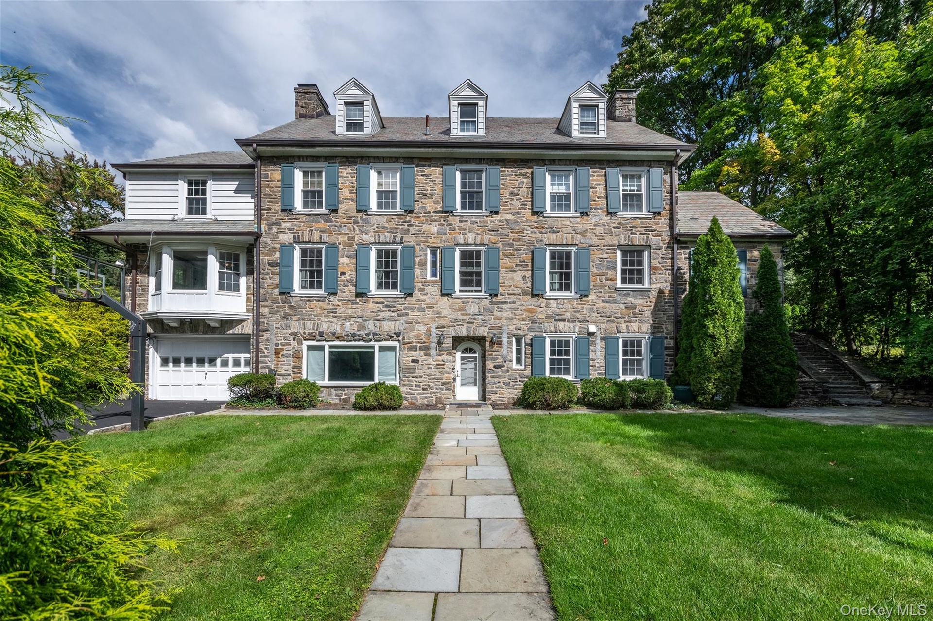 Stone facade residence with multiple dormer windows, a prominent walkway, and an attached two-car garage