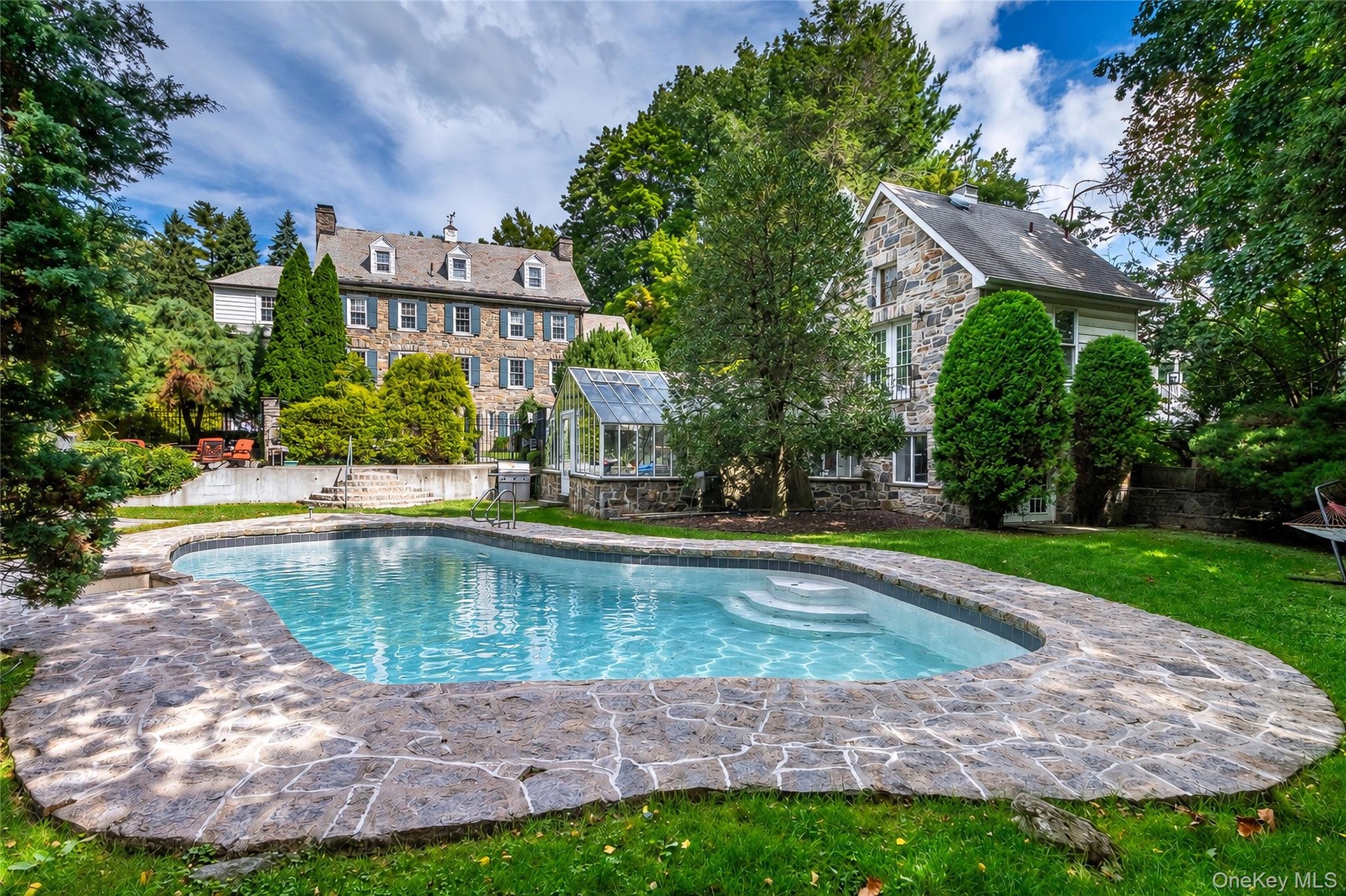 Curved swimming pool with integrated steps, surrounded by stone coping and a manicured lawn