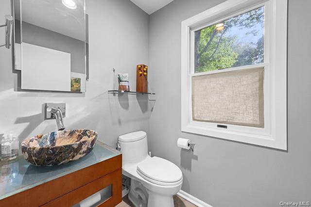 Vessel sink with a unique stone basin, wall-mounted faucet, wood-finish vanity, and a large window