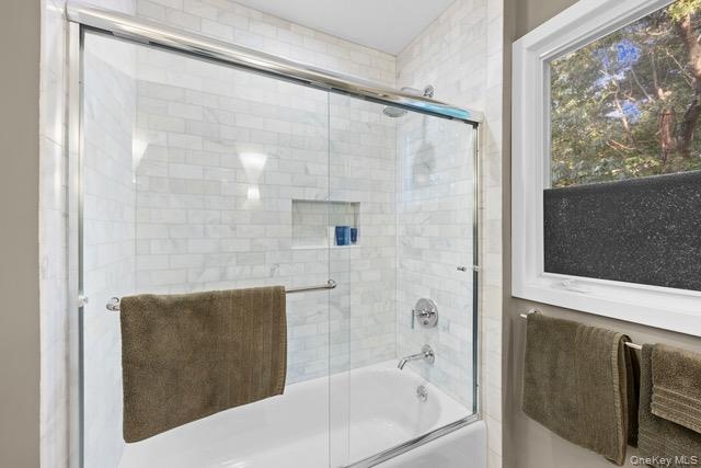 Tub-shower combination featuring subway tile surround, glass sliding door, and integrated shower niche