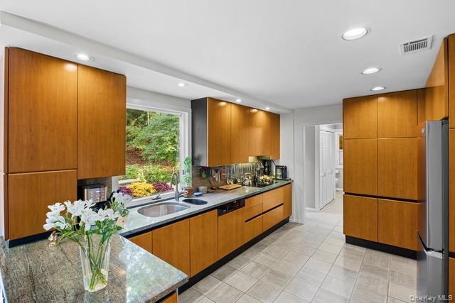 Sophisticated kitchen featuring warm wood-finish cabinetry with sleek black countertops, stainless steel appliances