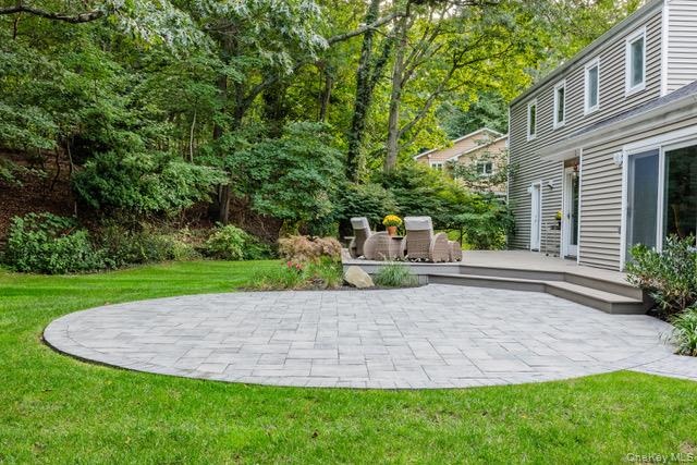 Expansive lawn with a circular paver patio, composite deck, and mature landscaping