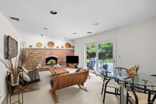Exposed brick fireplace with hearth, recessed lighting, carpeted flooring, and sliding glass door