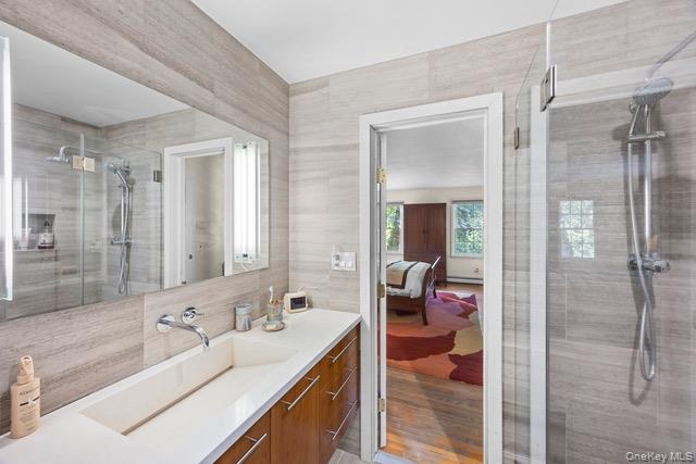 Bathroom featuring a frameless glass-enclosed shower, wall-mounted shower fixture, an integrated rectangular sink, wood-finish cabinetry, and a large 