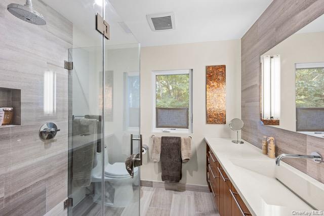 Full bathroom featuring a glass-enclosed shower with a rain showerhead, a built-in shower niche, a wood-finish vanity with an integrated rectangular s
