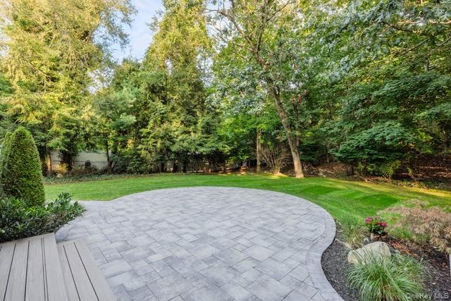Expansive backyard featuring a curved paver patio, lush green lawn, and mature trees