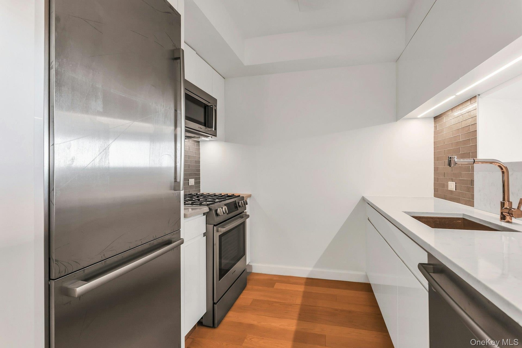 Kitchen with white cabinets, stainless steel appliances, light stone counters, and dark wood-style floors