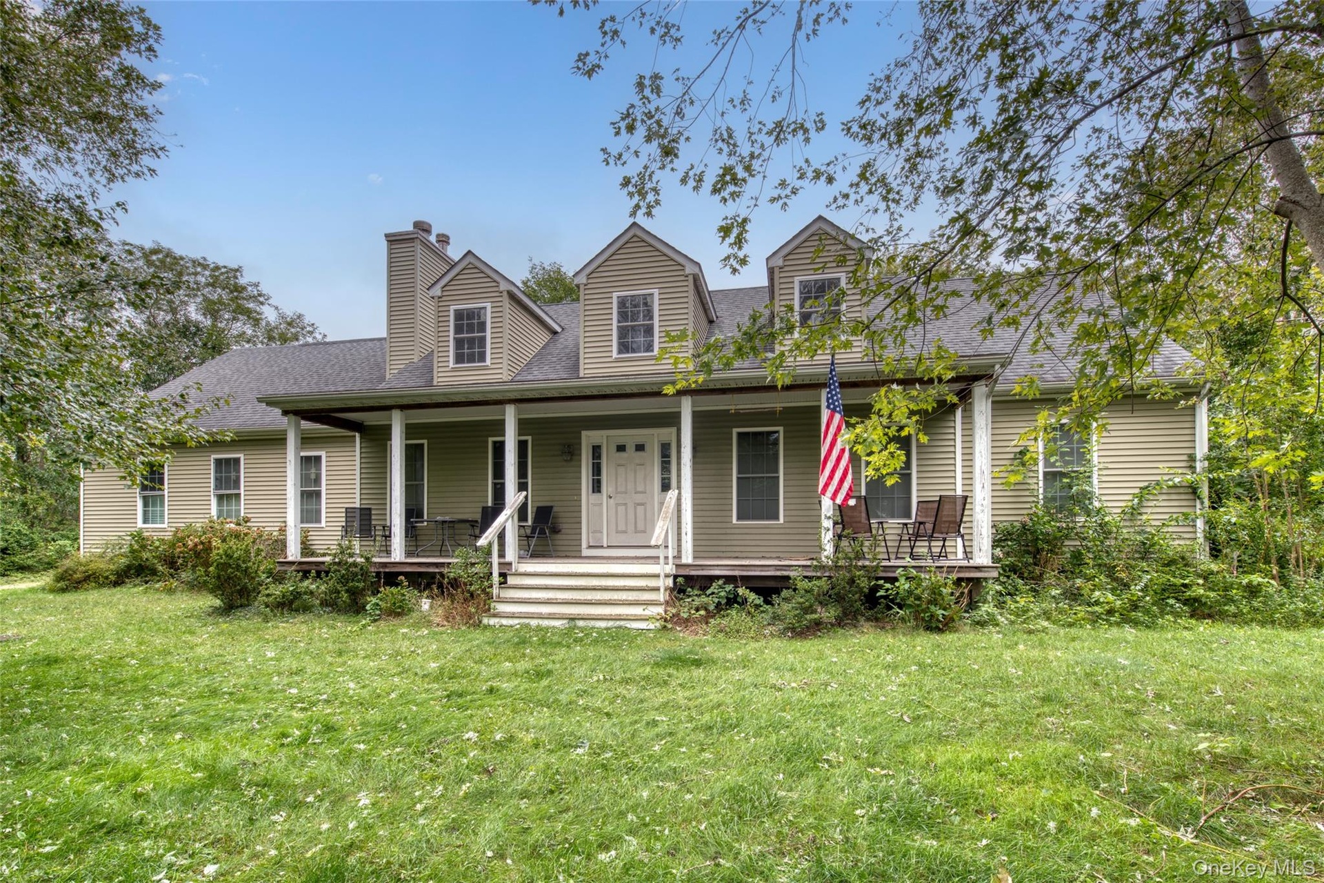 Expansive front lawn leading to a welcoming covered porch, dormer windows, and a prominent chimney