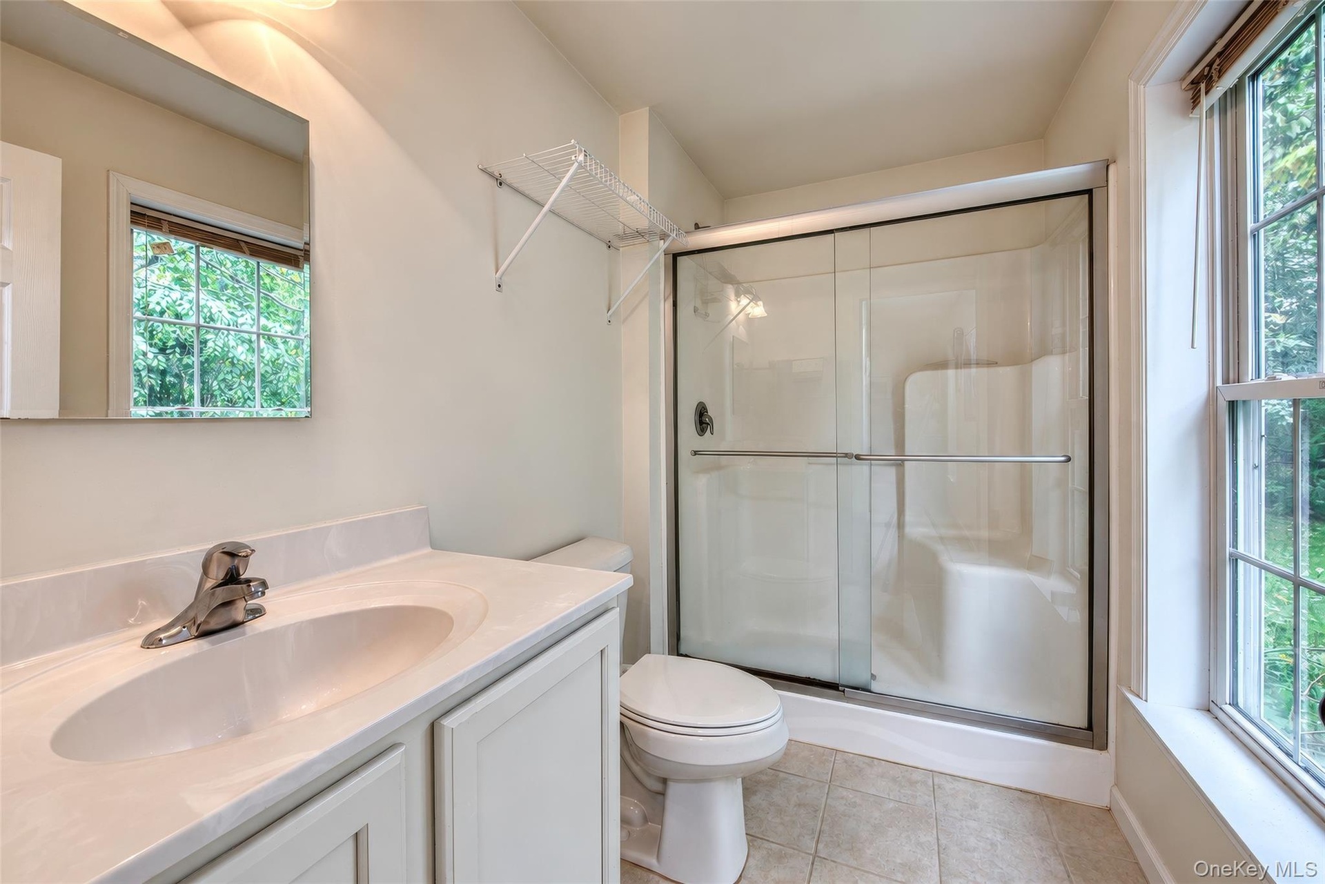 Bathroom featuring a vanity with an integrated sink, polished chrome faucet, a toilet, a shower with sliding glass doors, and a double-hung window