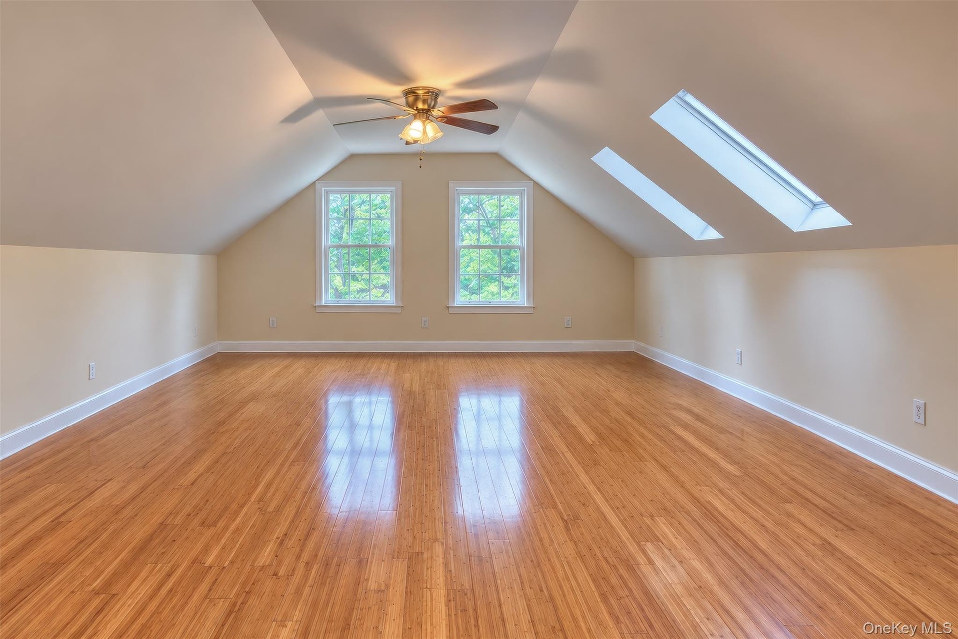Bedroom featuring wood-finish flooring, two large skylights, two double-hung windows, a ceiling fan with integrated lighting, and sloped ceilings