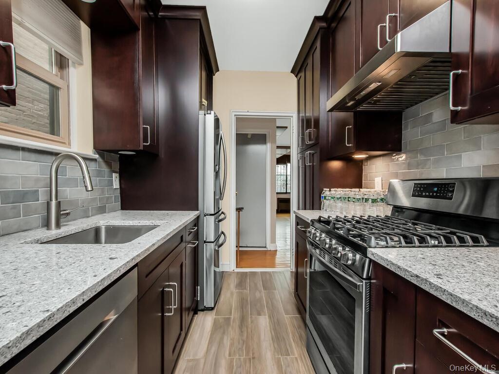 Kitchen with under cabinet range hood, a sink, tasteful backsplash, stainless steel appliances, and light stone countertops