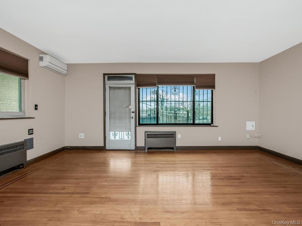 Empty room with an AC wall unit, light wood-style flooring, radiator, and baseboards