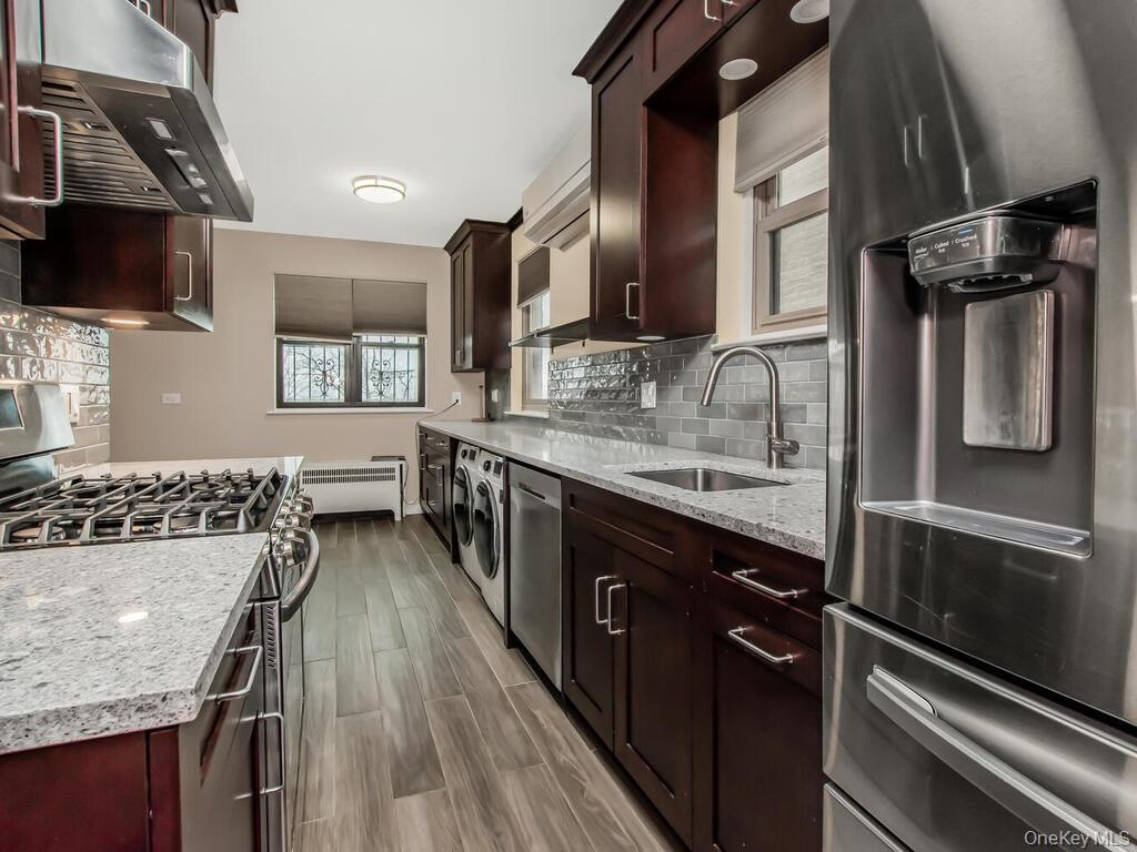 Kitchen with a sink, washing machine and dryer, range hood, radiator heating unit, and stainless steel appliances