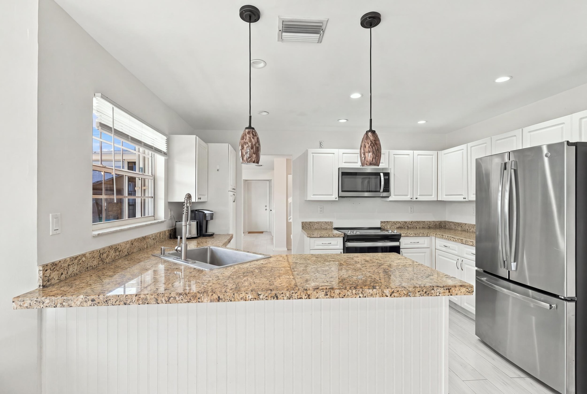 The bright eat-in kitchen features contemporary white cabinetry, granite countertops, new stainless steel appliances, and a convenient breakfast bar. 
