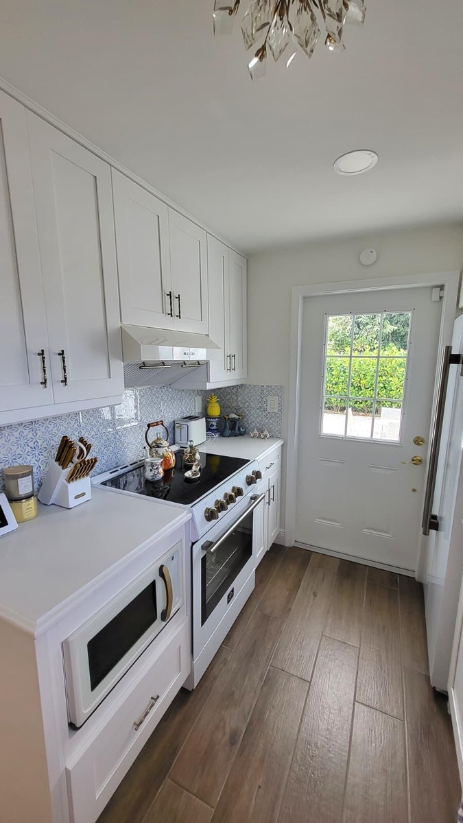 White cabinetry, light-toned countertops, full tile backsplash, wood-finish flooring, and a glass-paned door
