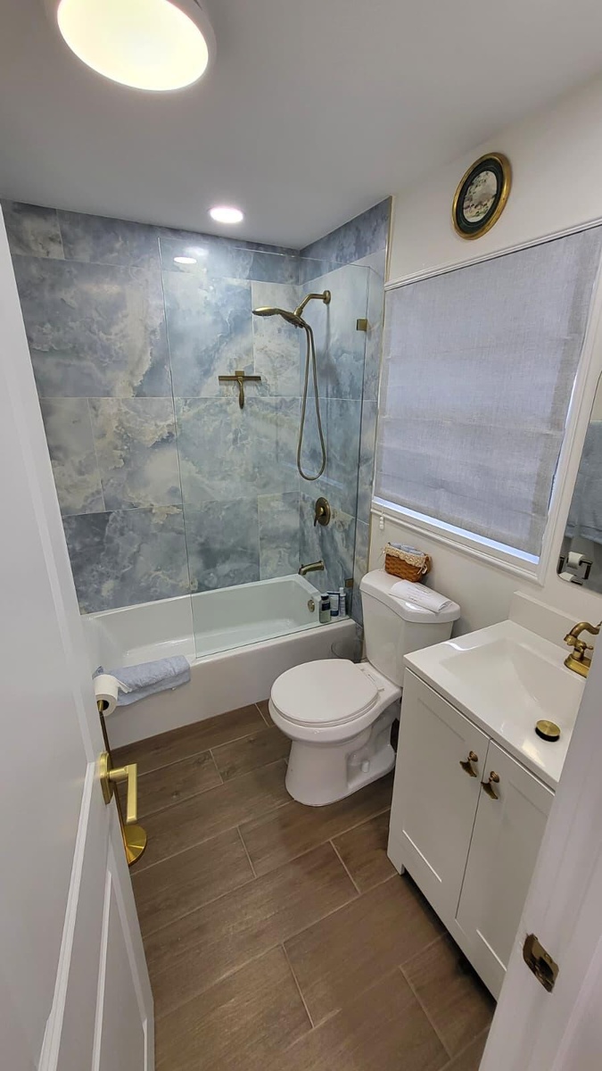 Bathroom featuring wood-finish flooring, a white vanity with integrated sink, a white bathtub, and a tiled shower surround