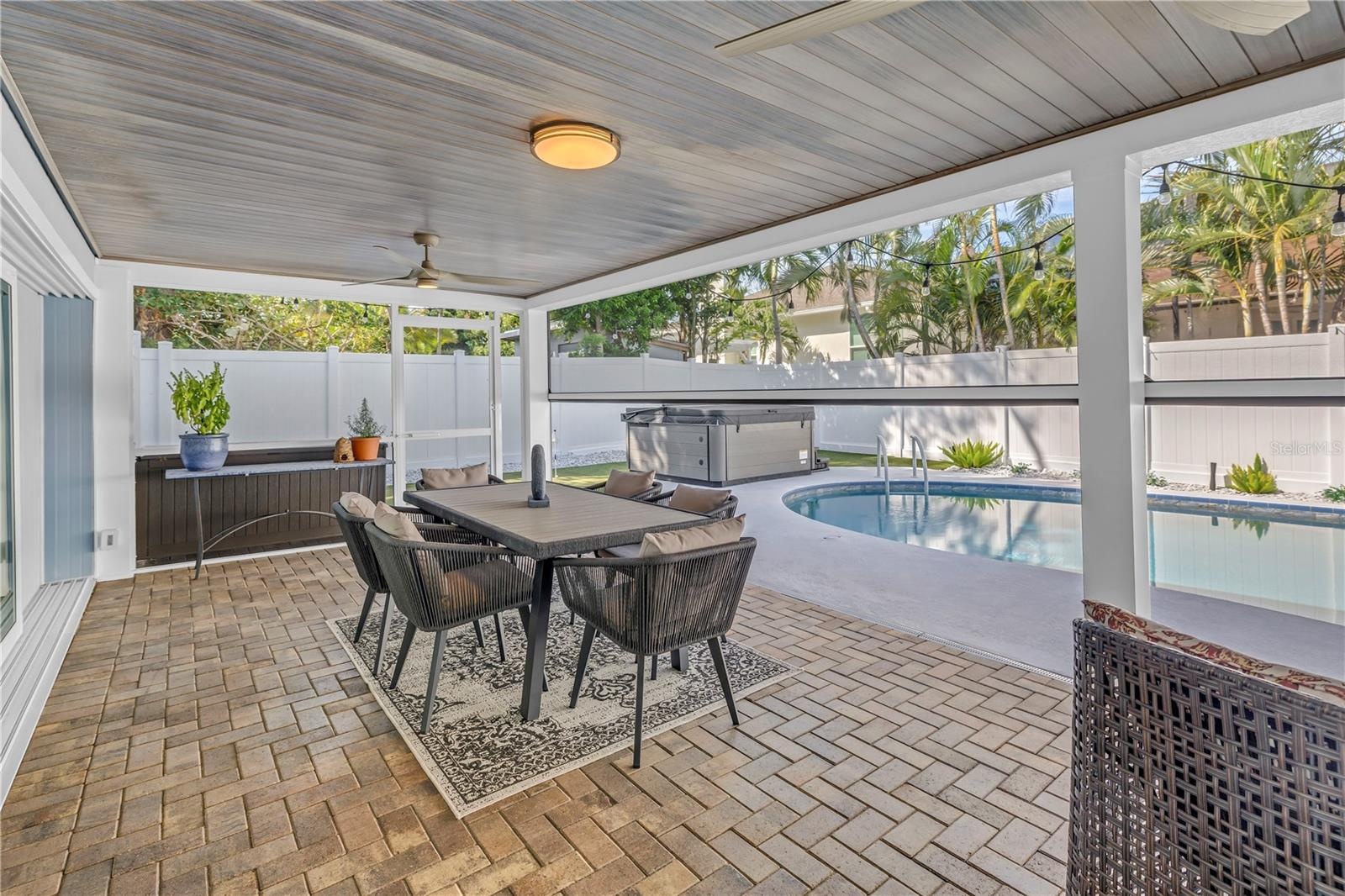 Paved patio with bead board ceiling for your outdoor Dining room with pool and HOT TUB beyond. Remote screens at half mast!
