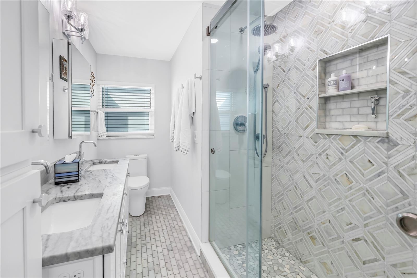 Primary bath with designer shower with spa stones and Art Deco influenced sand and sea aesthetic and built- in shower niche.