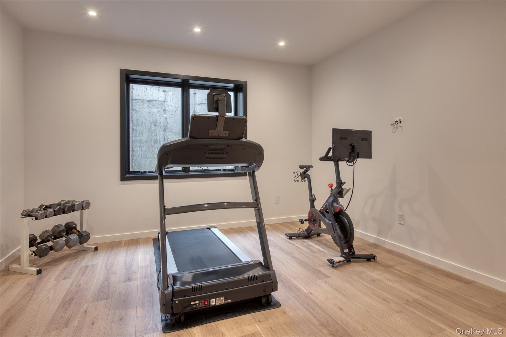 Recessed ceiling lighting illuminates the room with wood-finish flooring and a single window with a black frame