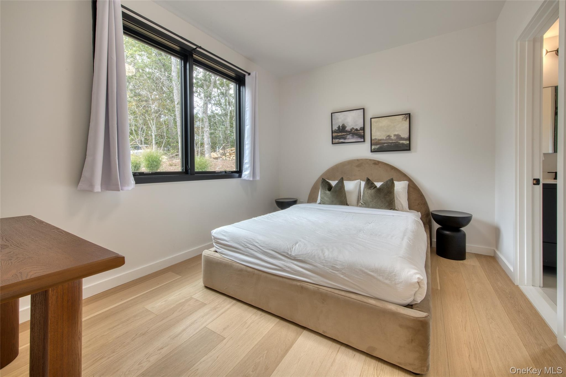 Bright room with wood-finish flooring, white walls, and a large window with black framing