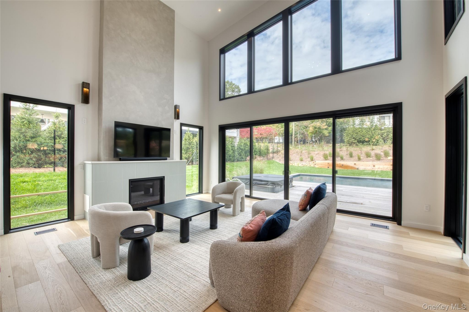 Two-story living area with high cathedral ceilings, featuring a built-in fireplace, large format windows, and wood-finish flooring