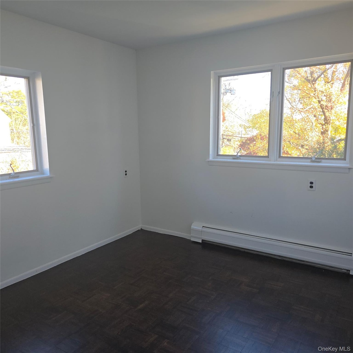 Unfurnished room with baseboard heating, a wealth of natural light, and dark parquet flooring