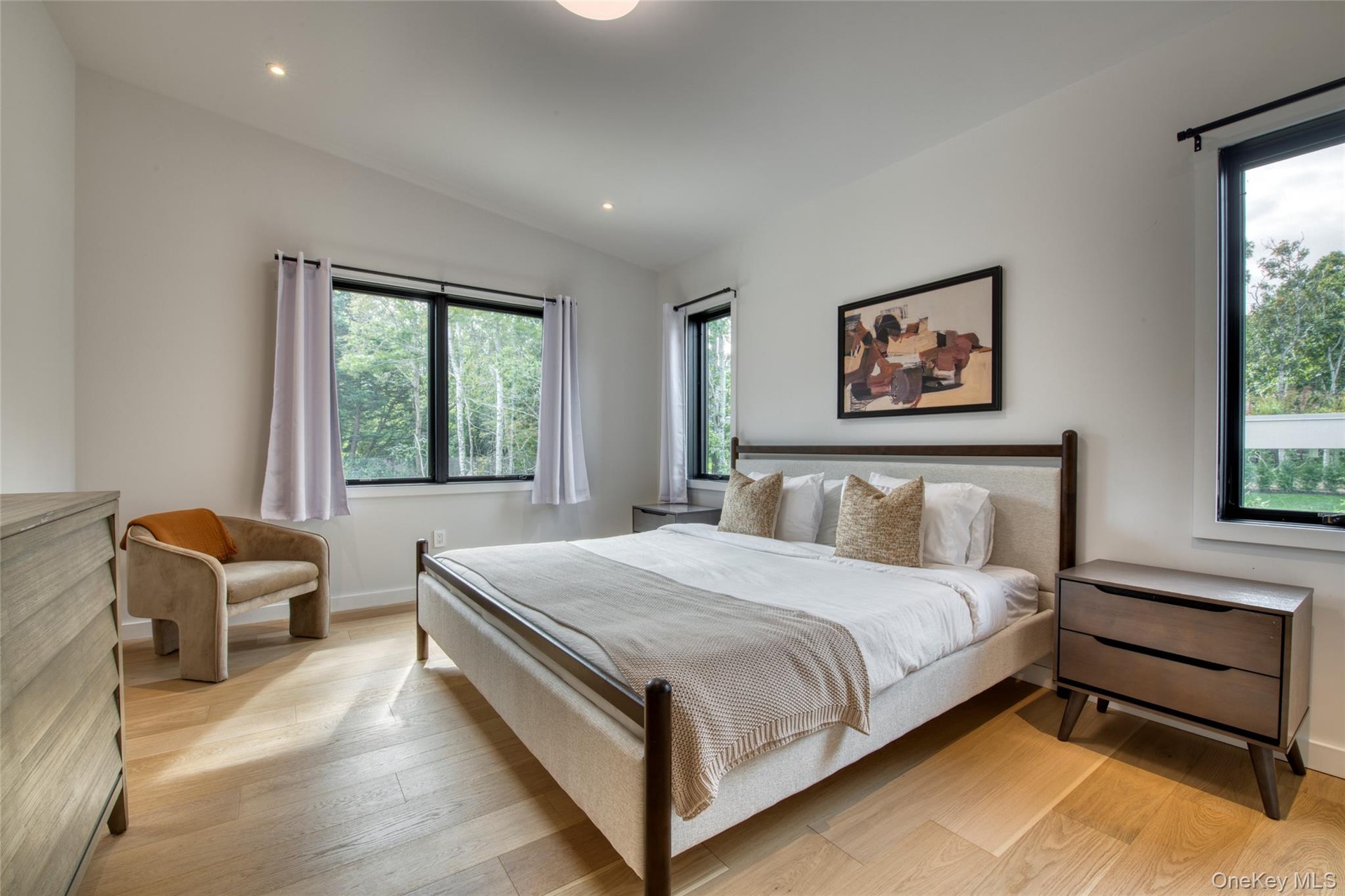 Vaulted ceiling with recessed lighting, wood-finish flooring, and multiple windows with dark trim