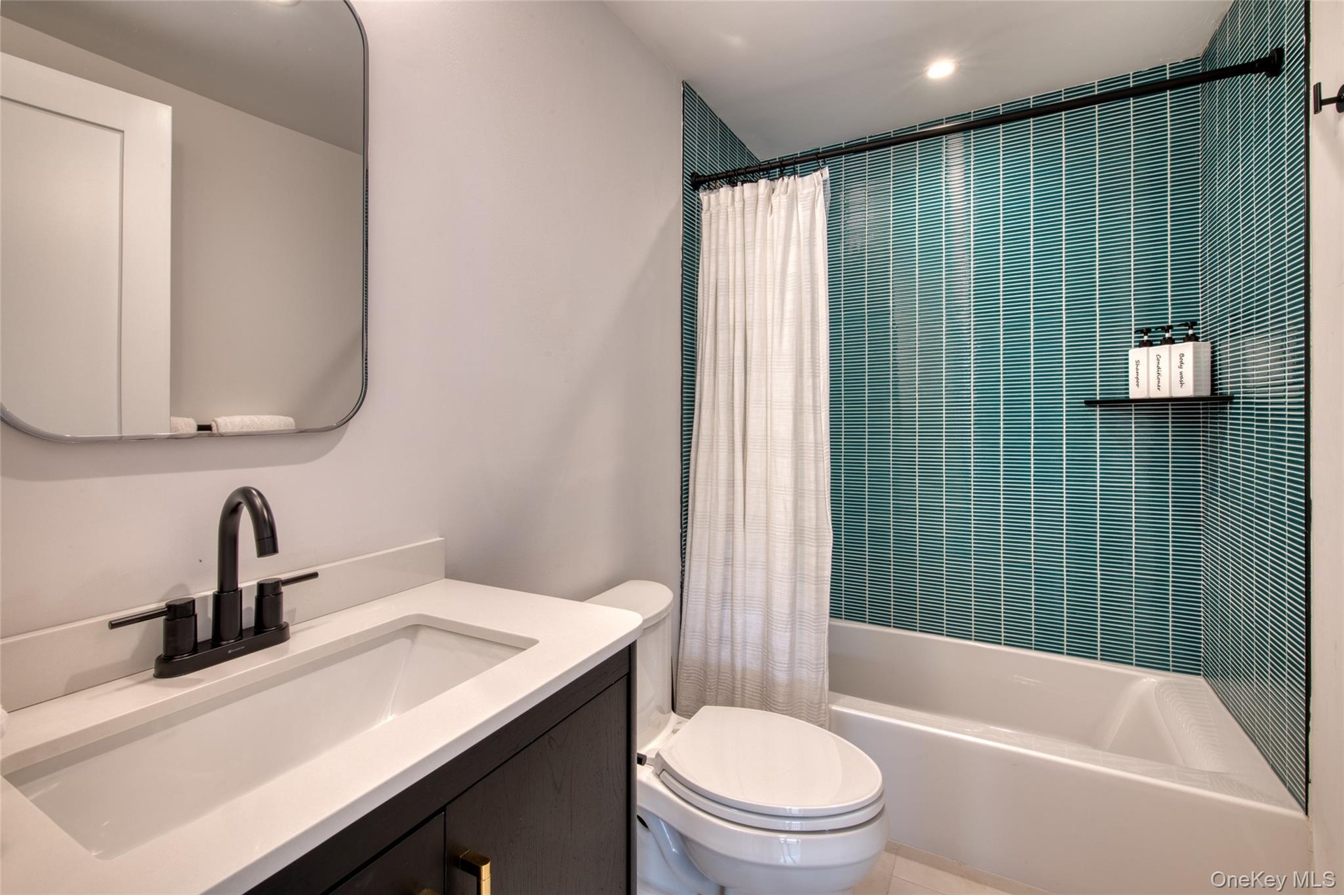 Bathroom featuring a dark wood-finish vanity with a white countertop and rectangular sink, matte black faucet, and a shower/tub combination with teal 