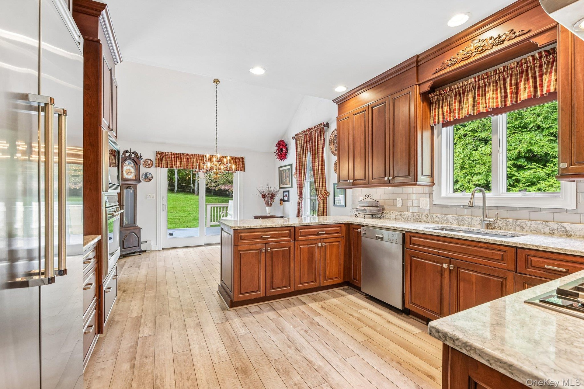 Spacious kitchen featuring wood-finish flooring, wood cabinetry, light-toned countertops, stainless steel appliances, and a vaulted ceiling