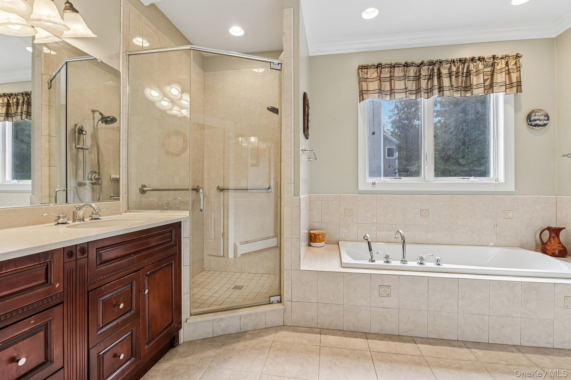 Built-in jetted tub with tile surround, corner glass-enclosed shower with tile, dark wood-finish vanity with countertop, undermount sink, and recessed