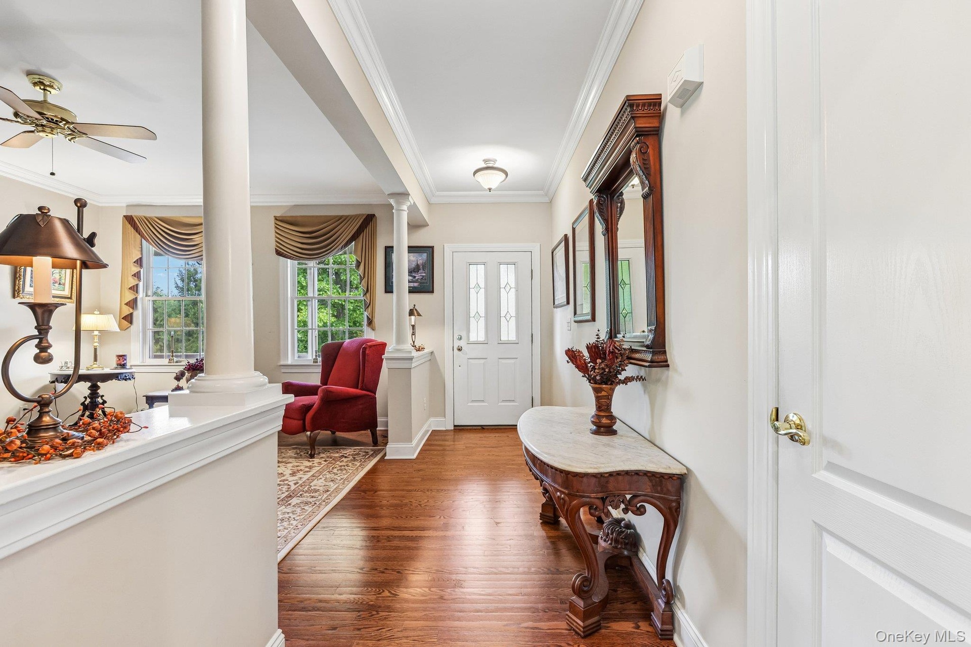 Hardwood flooring, decorative columns, crown molding, transom window above entry, and a ceiling fan